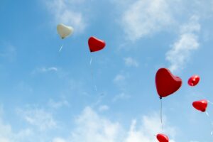 Red and white heart shaped balloons against a blue sky with faint white clouds
