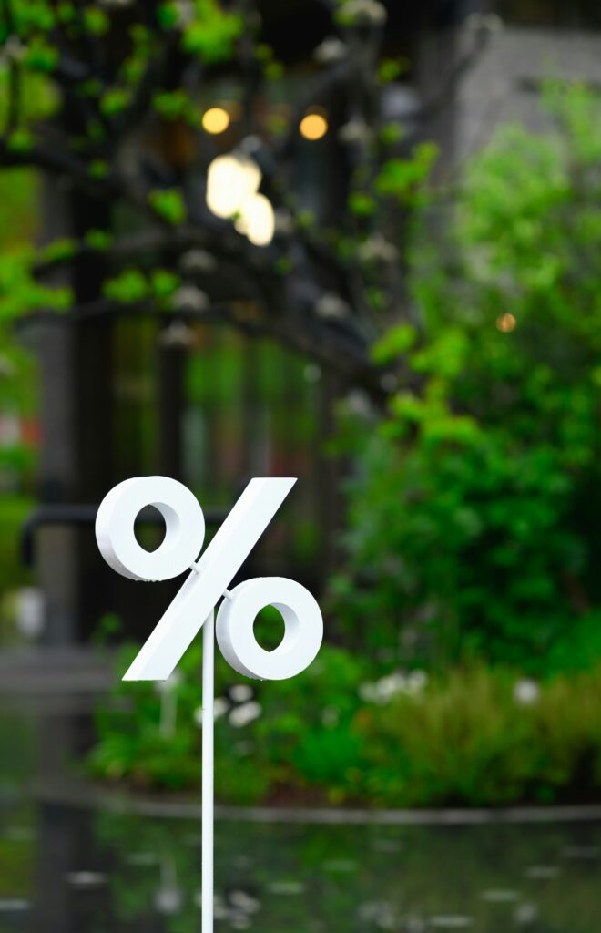 Big white percentage sign in the foreground with a blurred green park background