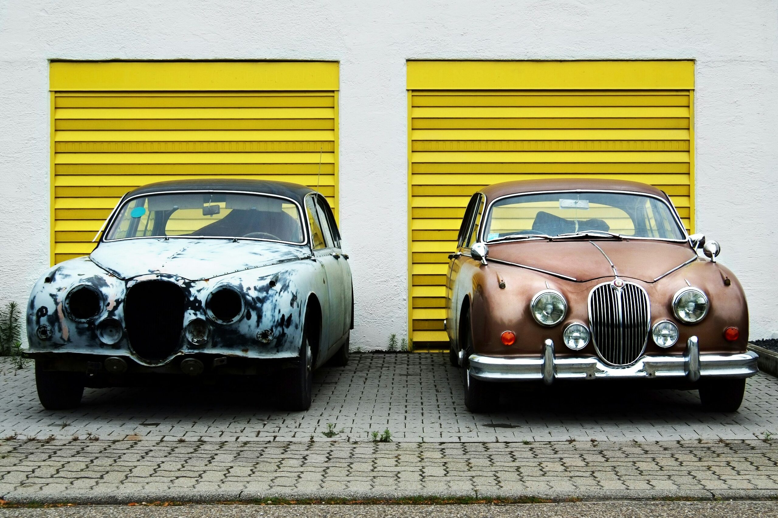 Retro cars in different state of repairs in front of yellow garage doors