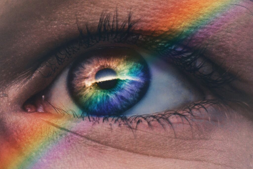 Close up of a blue eye with a transparent rainbow glow diagonally across